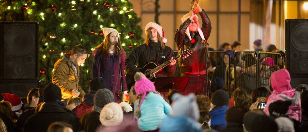 musicians and singers in front of lit Christmas tree with crowd