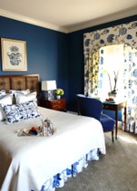 room with white linens and blue walls with floral curtain